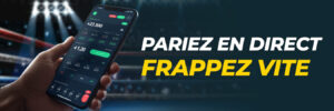 Main tenant un smartphone avec une application de paris en direct dans un ring de boxe éclairé.